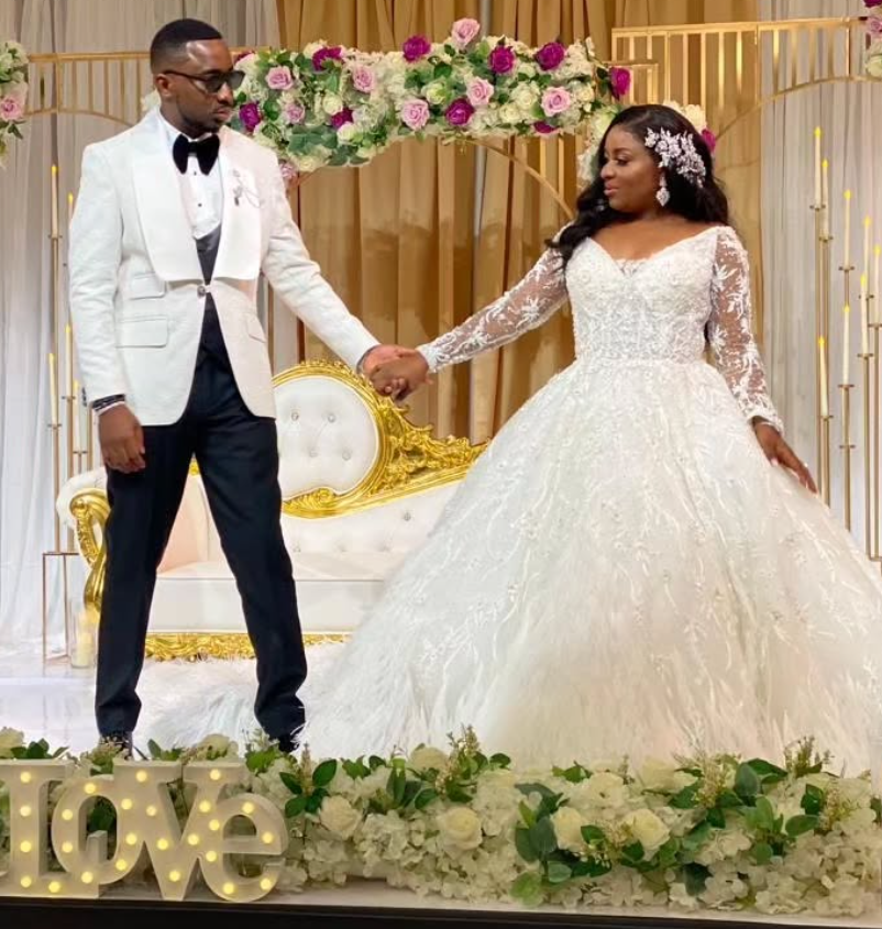 A bride and groom hold hands in front of a love sign