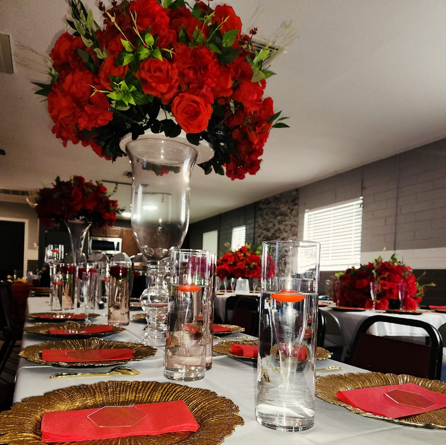 A table set for a wedding reception with a vase of red flowers hanging from the ceiling