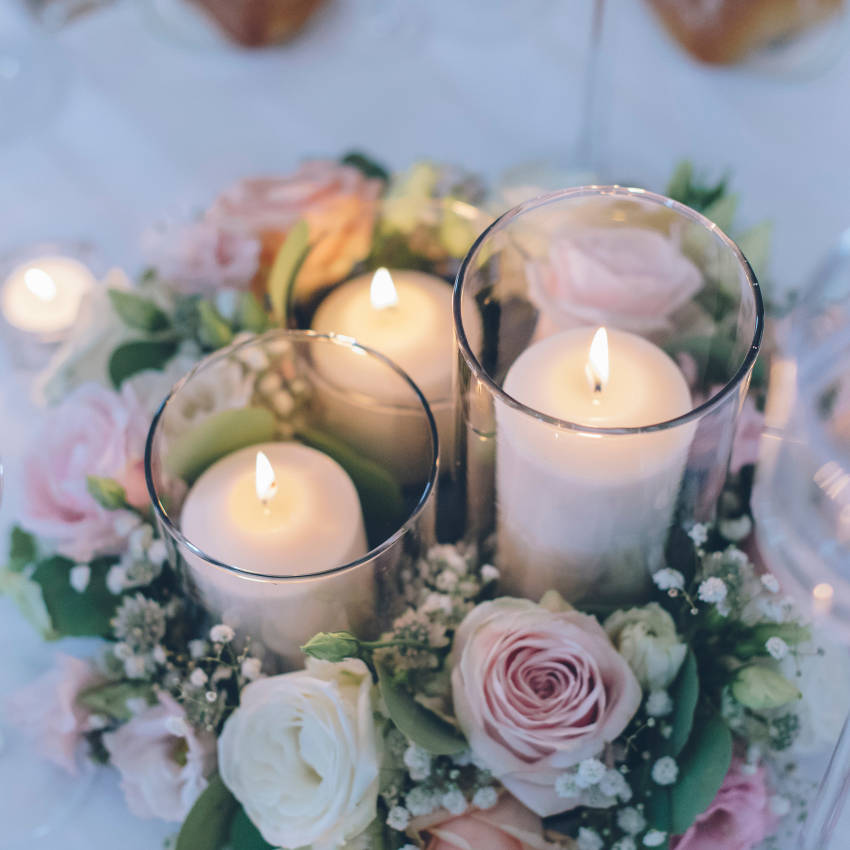 Three candles in glasses surrounded by pink roses and baby 's breath