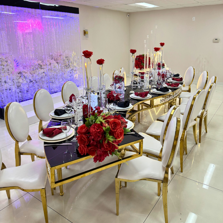 A long dining table with red flowers and candles on it.