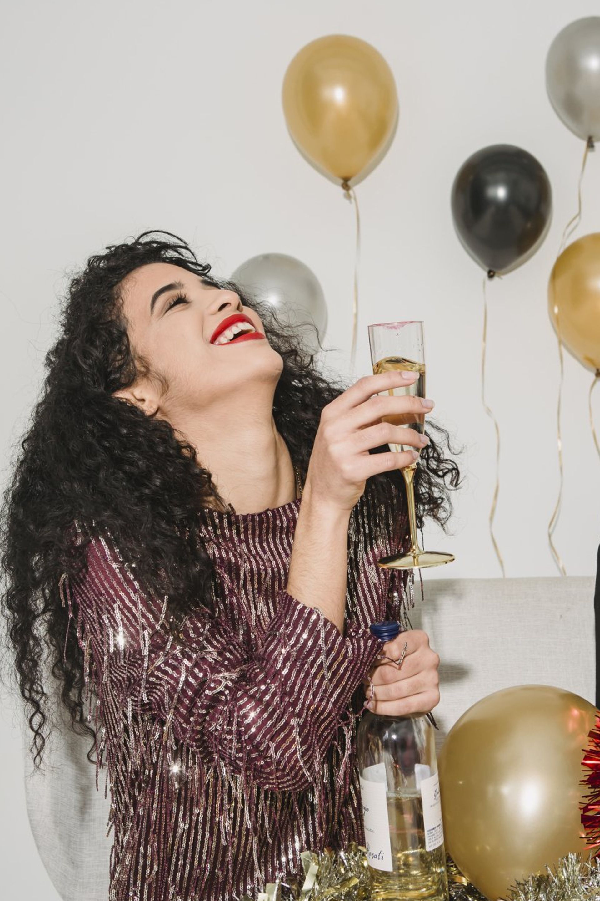 A woman is holding a glass of champagne and a bottle of wine at a party.