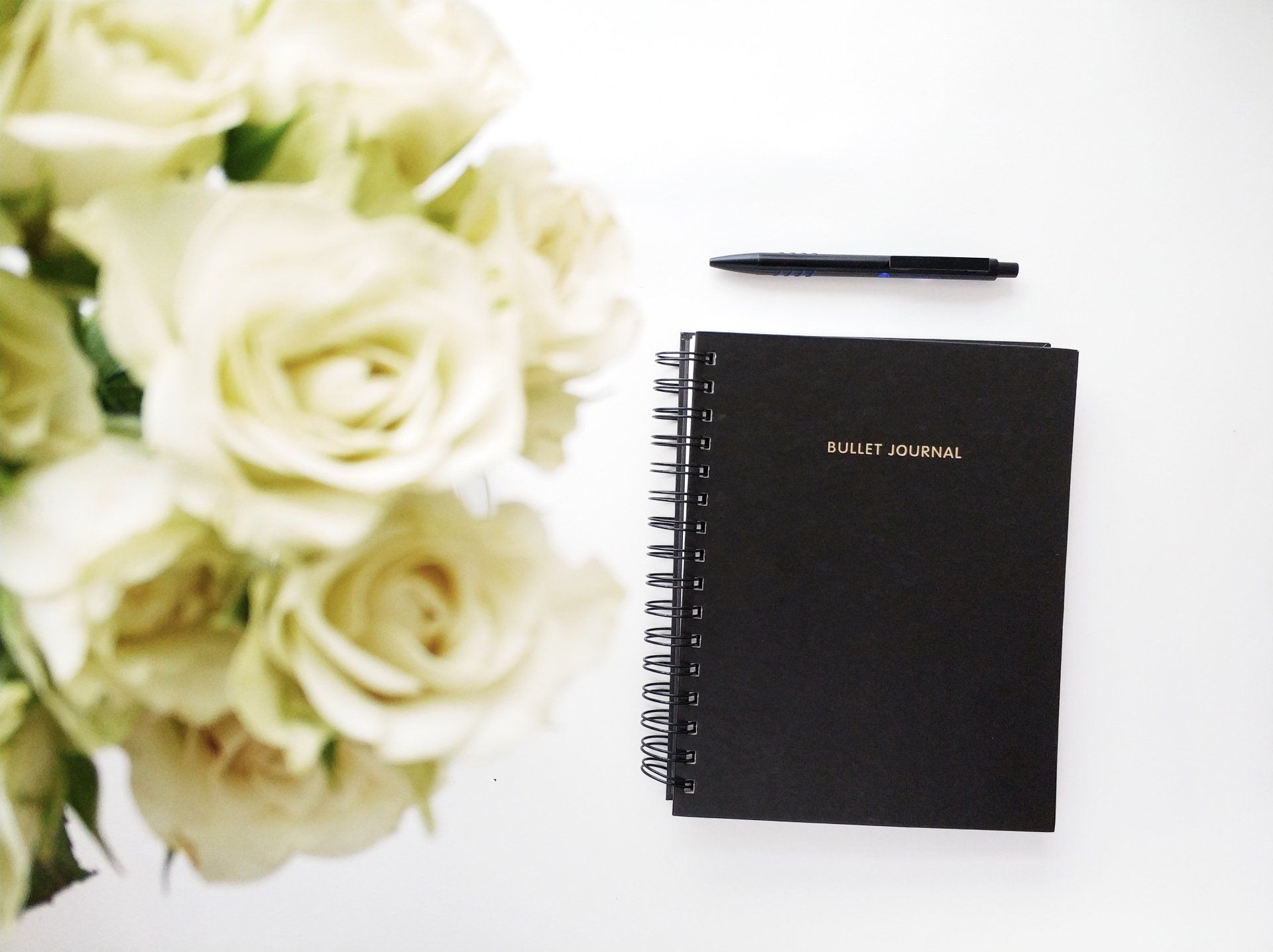 A bouquet of white roses sits next to a black spiral notebook
