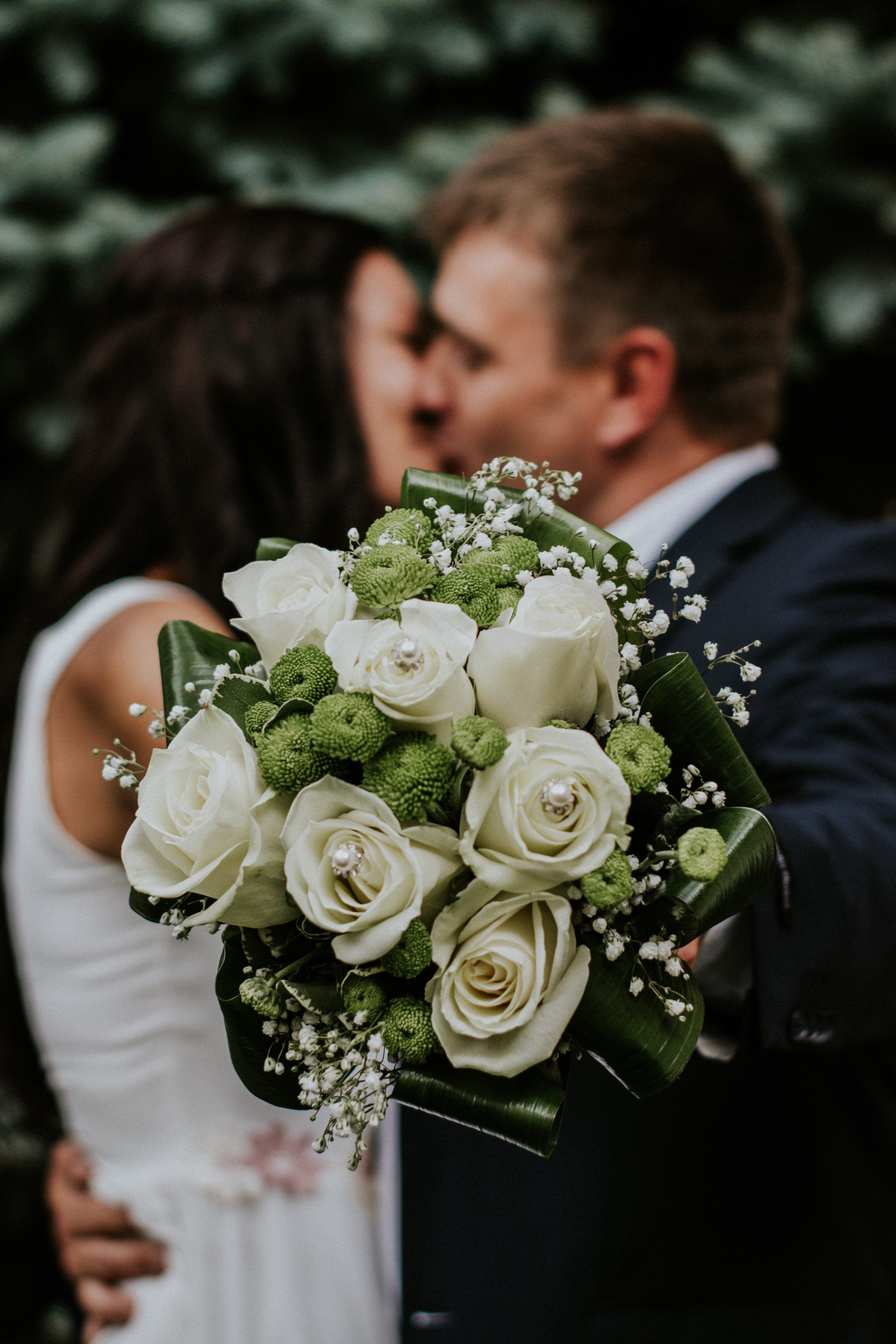 A bride and groom kissing while holding a bouquet of white roses.